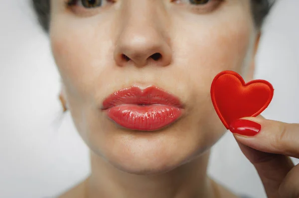 Part of womans face. Small red heart near womans lips. Kiss. Red nails.