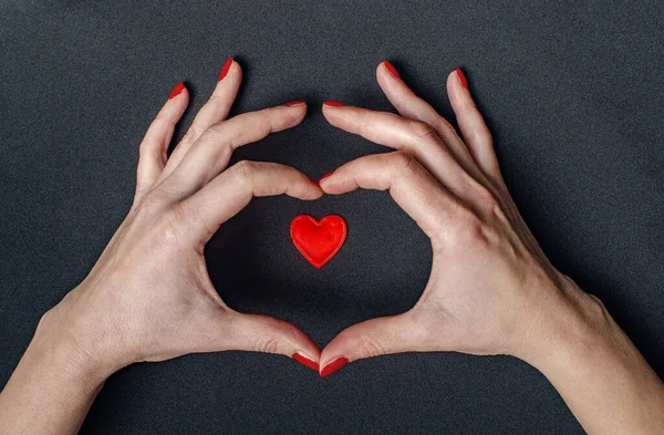 Female hands around red heart. Love. Black background. Red nail polish