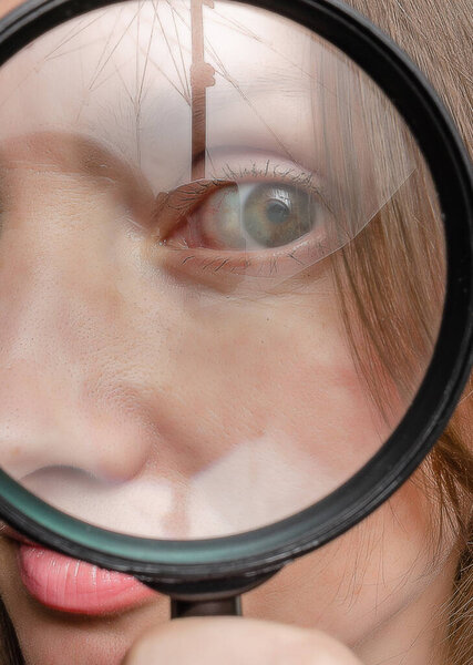 Adult woman's eye seen through magnifying glass. Reflections. Mystery