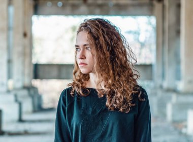 Charming sexy cute woman with wavy hair. Blurred background of abandoned old building.