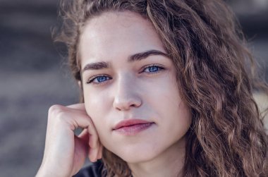 Attractive face of young woman with wavy hair. Blue eyes, black eyebrows, smile.