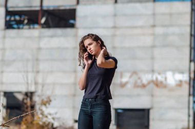 Sexy slender woman is talking on mobile phone. Black T-shirt and jeans. Blurred background.