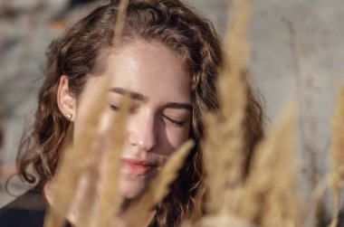 Face of woman dreaming with closed eyes in field grass, dry flowers. Curly hair. Autumn