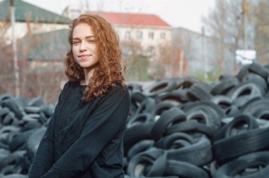 Cute girl with curly dark hair is laughing. Tire dump background