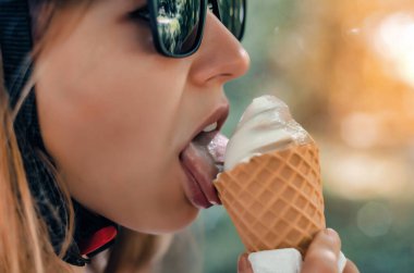 Siyah gözlüklü kız dondurma külahını yalıyor.