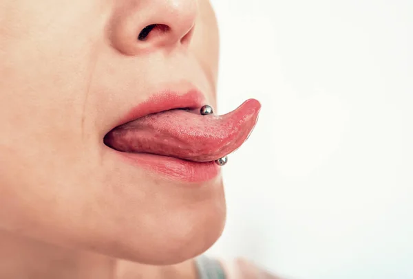 Piercing on the tongue of woman. Side view of woman's mouth with tongue sticking out.