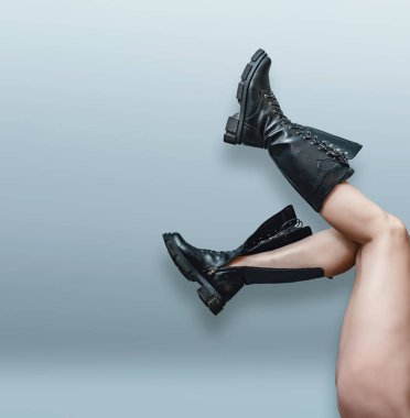 Gri arka planda siyah botlarla büyüyen kadın bacakları..