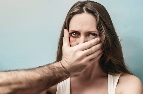 Male hand covers mouth of a scared woman close up. Domestic violence, abduction. Mature woman with bruise near eye and male hand on face on isolated background.