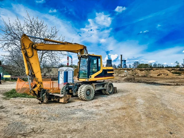Yellow excavator on an earthen construction site in industrial zone