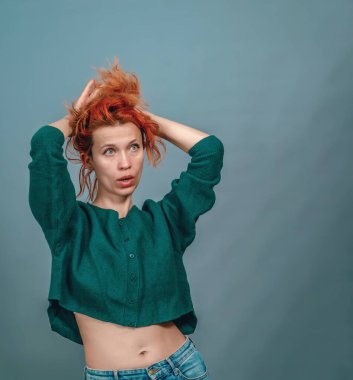 Şaşırmış kadın yana bakıyor, elleriyle saçlarını kaldırıyor. Kısa çıplak göbek kazağı.