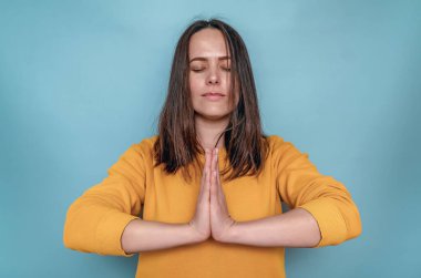 Koyu renk düz saçlı kadın kollarını göğsünün önünde katlamış. Meditasyon. Mavi arkaplan