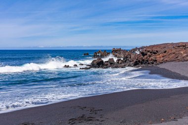 Kum ve siyah katı lav ile kıyıya vuran dalgaların beyaz deniz köpüğünün parlak kontrastı.