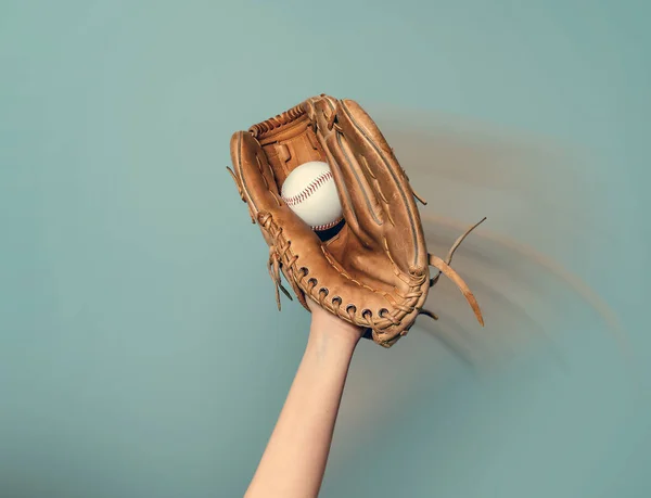 A baseball glove on his hand catches white game ball