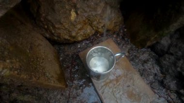 Pınarın dibinde metal bardak. Bir su akıntısı metal bardağa dökülür.