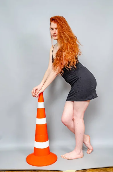 黒のドレスの赤い髪の女性は灰色の背景に道路標識とポーズをとります 警告サイン — ストック写真