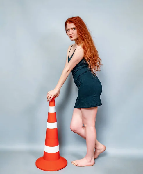 黒のドレスの赤い髪の女性は灰色の背景に道路標識とポーズをとります 警告サイン — ストック写真