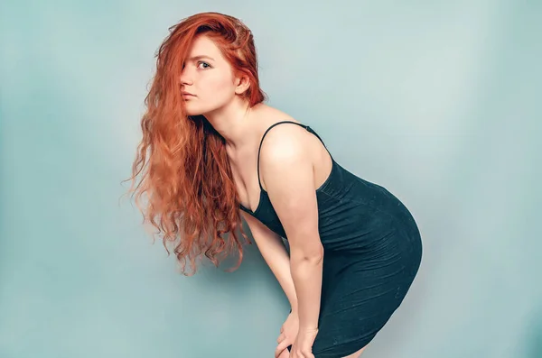 Amazing red-haired woman in black short dress posing on gray background. Studio photo