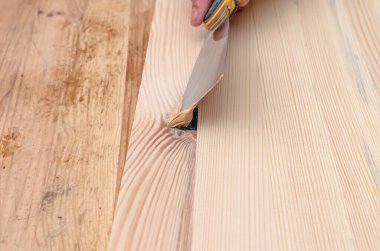 Tahtadaki düğümleri macunla kapatmak. Spatula, macun, tahta tahta. Marangozun elleri..