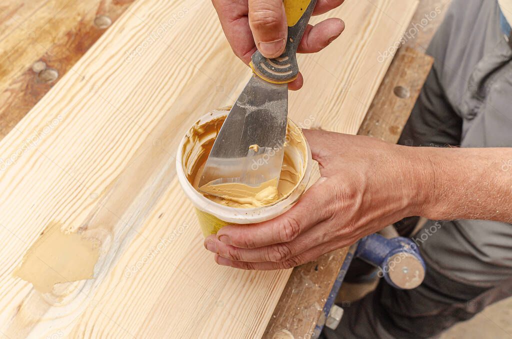 Carpenter uses putty to smooth out the knots in a wooden board. Recovery background.