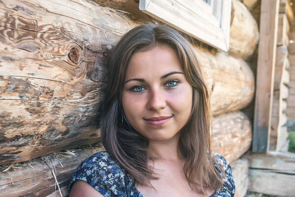 A pretty Slavic girl sits near a wooden house. Close-up portrait, home comfort