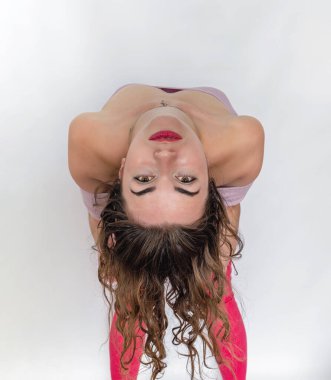 Kadın stüdyoda poz veriyor, arkasına yaslanıyor. Parlak makyajlı ters yüz, dalgalı saçlar.