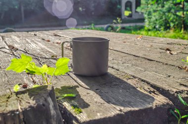 Dışarıdaki ahşap bir masada, güneş ışınlarında metal turist kupası.