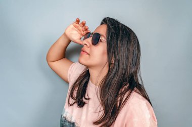 Siyah saçlı, güneş gözlüğü takan bir kadın. Yüze yakın el