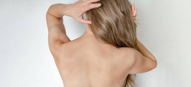 İnce kadın sırtı kameraya dönük duruyor, tarıyor, saçını düzleştiriyor.