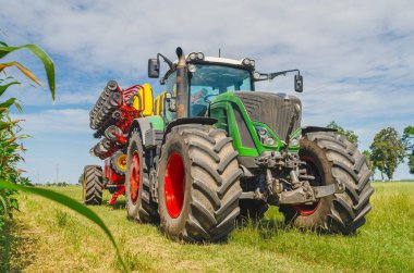 Tarım yazının aydınlık manzarası. Mısır tarlasının yakınındaki büyük ekicinin arkasında bulutlar var.