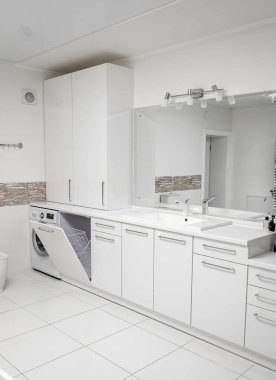Banyodaki beyaz mobilyalar. Komodin, çamaşır makinesi, ayna.