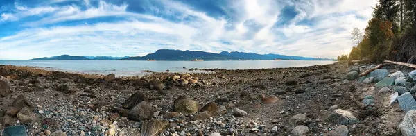 Panoramic photo of the sea bay with a view of the mountains and the city on the horizon under a cloudy sky