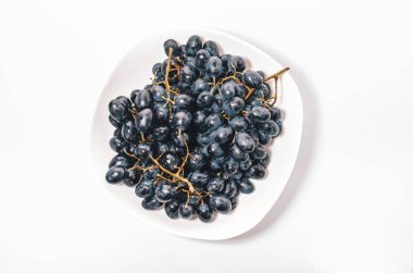 Beyaz arka planda beyaz bir tabakta bir sürü mavi üzüm. Böğürtlen, yaz hasadı, sağlıklı yemek.