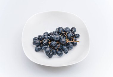 Beyaz arka planda beyaz bir tabakta bir sürü mavi üzüm. Böğürtlen, yaz hasadı, sağlıklı yemek.