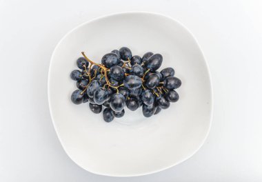 Beyaz arka planda beyaz bir tabakta bir sürü mavi üzüm. Böğürtlen, yaz hasadı, sağlıklı yemek.