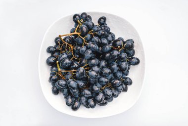 Beyaz arka planda, beyaz tabakta bir sürü mavi üzüm. Böğürtlen, yaz hasadı, sağlıklı yemek.