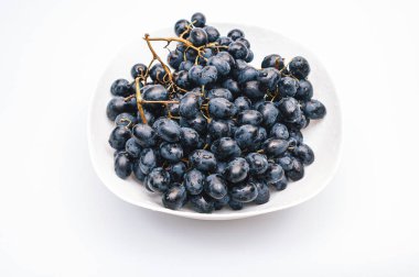 Beyaz arka planda, beyaz tabakta bir sürü mavi üzüm. Böğürtlen, yaz hasadı, sağlıklı yemek.