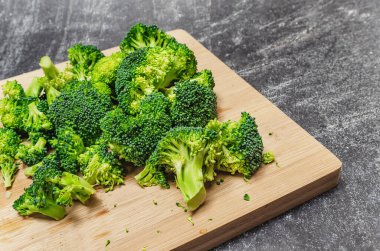 Tahta bir tahtanın üzerinde çiçeklere ayrılmış taze yeşil brokoli. Gri modern arkaplan