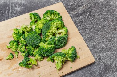 Tahta bir tahtanın üzerinde çiçeklere ayrılmış taze yeşil brokoli. Gri modern arkaplan