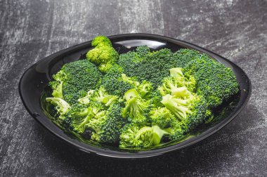 Taze yeşil brokoli çiçekleri siyah kasede gri arka planda izole edilmiş.