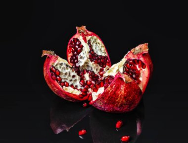 Sliced whole red pomegranate on shiny background. Reflections of pomegranate fruits