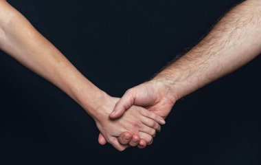 Bir kadının eli bir erkeğin elini tutar. Siyah bir arka planda el ele tutuşmak
