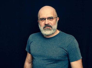 Gri sakallı kel bir adamın portresi. Orta yaşlı bir adam kameraya bakar.