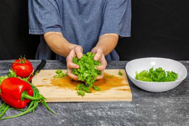 Beyaz kasenin yanında yeşil salata yaprakları var. Mavi tişört, siyah arka plan. Parlak sebzeler