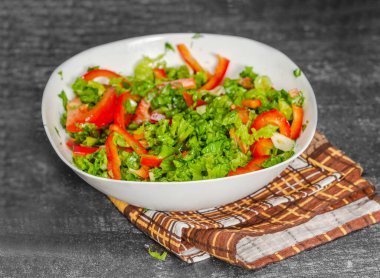 Kahverengi mutfak havlusunun üzerinde beyaz kase lezzetli sebze salatası duruyor. Gri arkaplan.