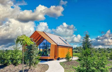 Mavi gökyüzünün altında patikası, ağaçları ve çalıları olan küçük bir ahır evi.