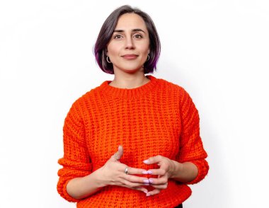 Çekici, neşeli, siyah saçlı, gülümseyen kadın. Turuncu örülmüş kalın bir kazak. Eller göğsün önünde..
