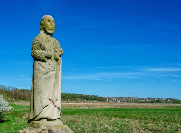 Stone statue Jesus Christ standing with palm branch in field under blue sky. Ancient architecture