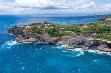 Gökyüzü ve bulutlarla harmanlanmış, gök mavisi okyanusun kenarında bir uçurum görünüyor. Doğal kıyı manzarası kayalık arazide bitki örtüsü barındırır.