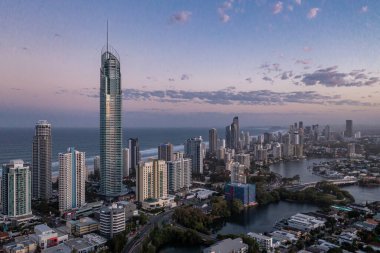 Günbatımında okyanusla birlikte modern şehrin insansız hava aracı görüntüsü. Turizm ve seyahat. Altın Sahil, Queensland Avustralya