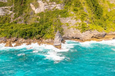 Yeşil tropikal bitki örtülü yüksek kayalar, köpüklü deniz suyu. İHA tipi. Bali, Klungkung, Endonezya